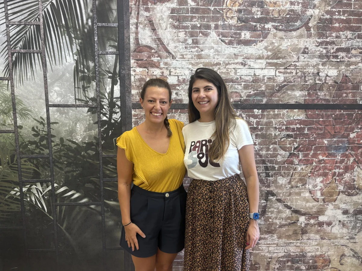 Dos mujeres de la comunidad Oceanworking sonríen ante una pared de ladrillo