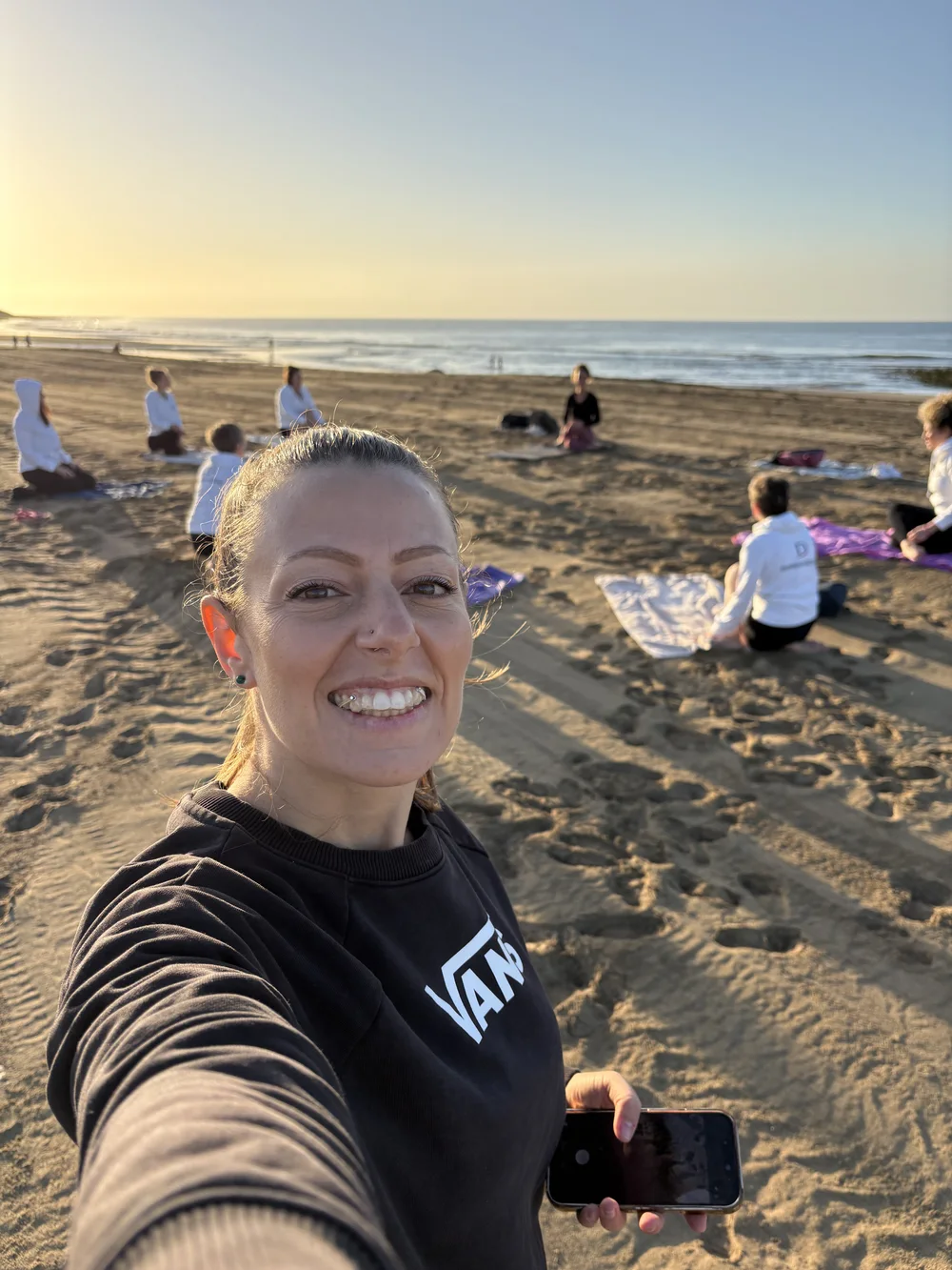 Mujer sonriente se hace un selfie ante una sesión de yoga en grupo en una playa de Gran Canaria al amanecer
