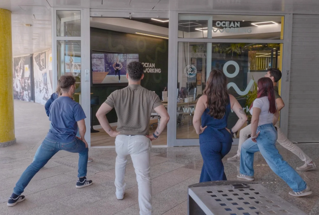 Grupo de personas en una sesión de movimiento al aire libre frente al ventanal del coworking Oceanworking