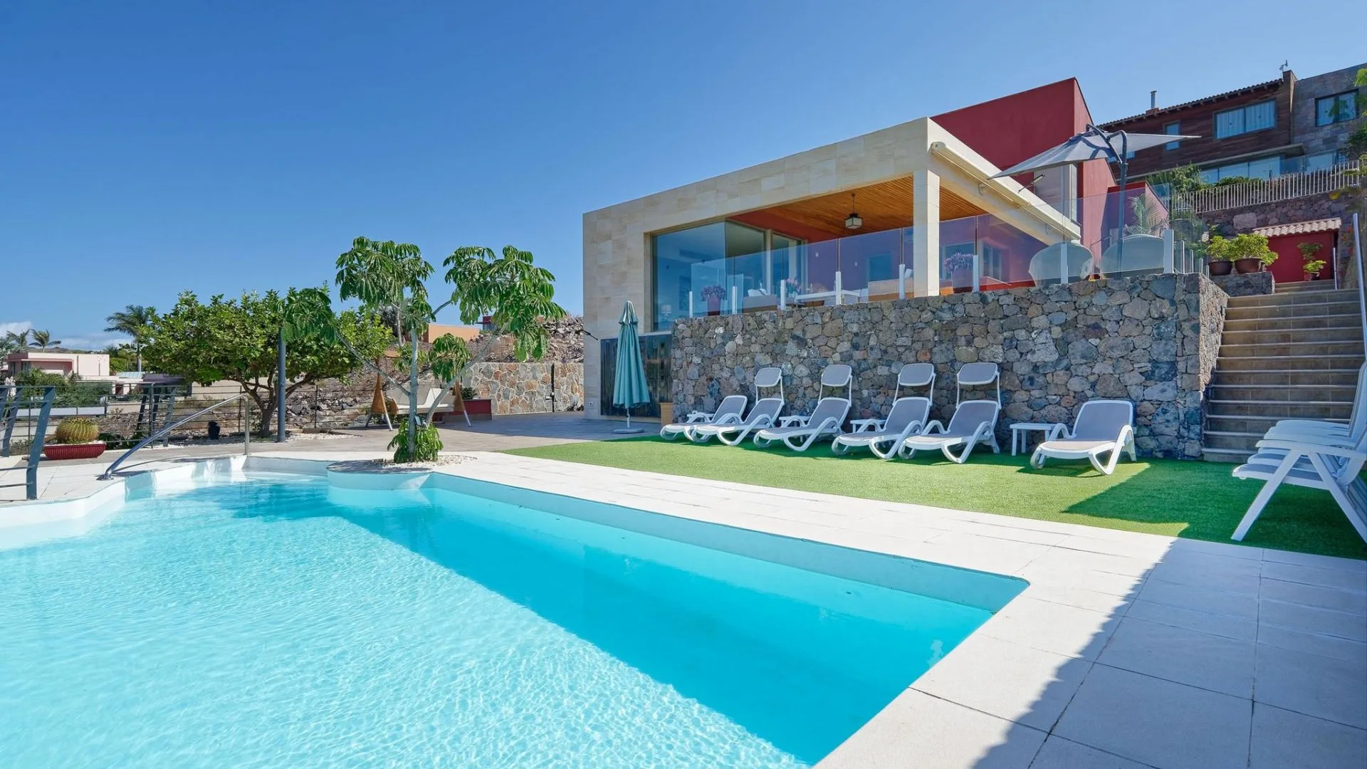 Villa de coliving con piscina, tumbonas y salón acristalado bajo un cielo azul en Gran Canaria