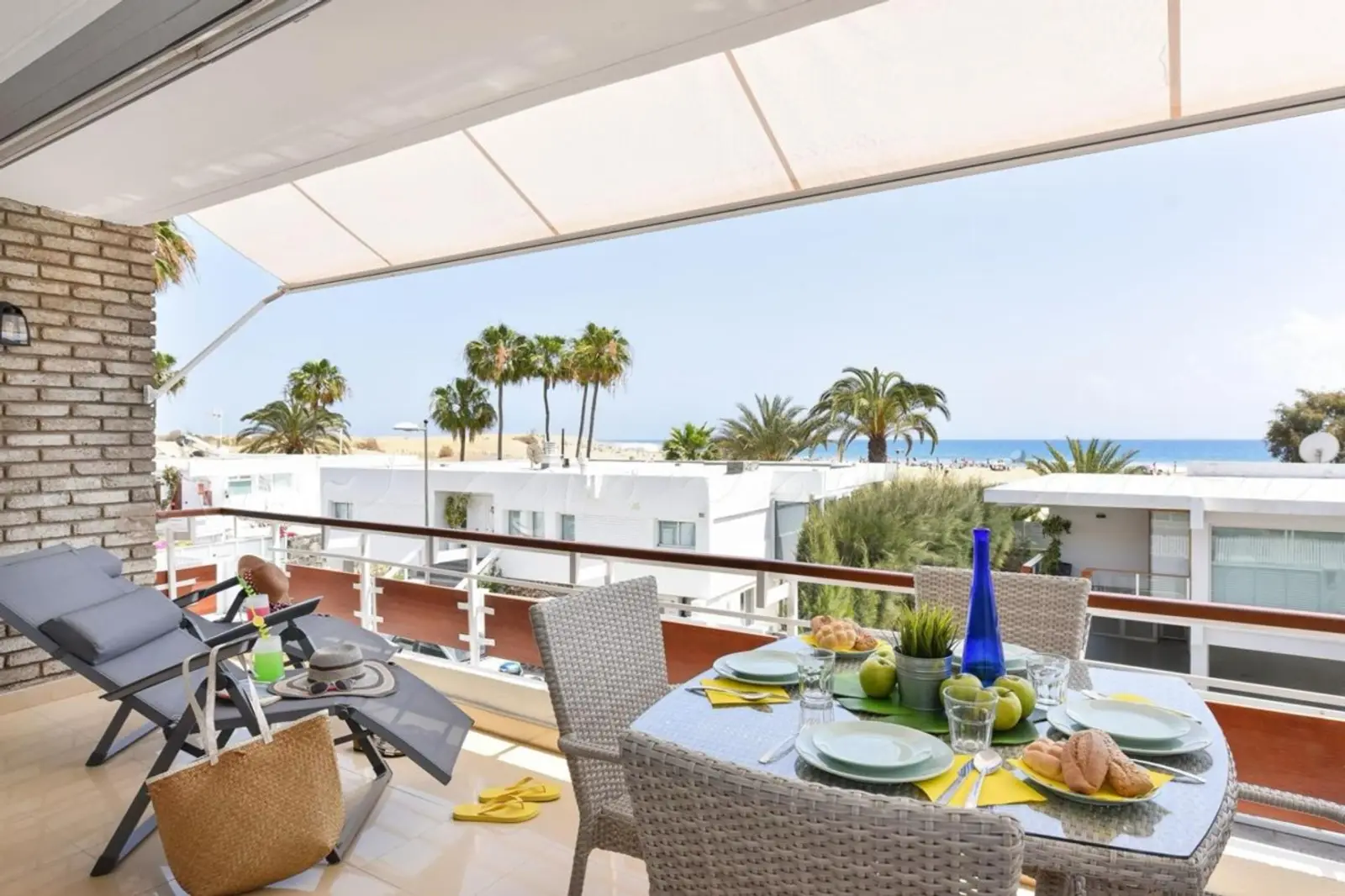 Terraza con mesa puesta y tumbonas frente a las palmeras y el mar en Maspalomas