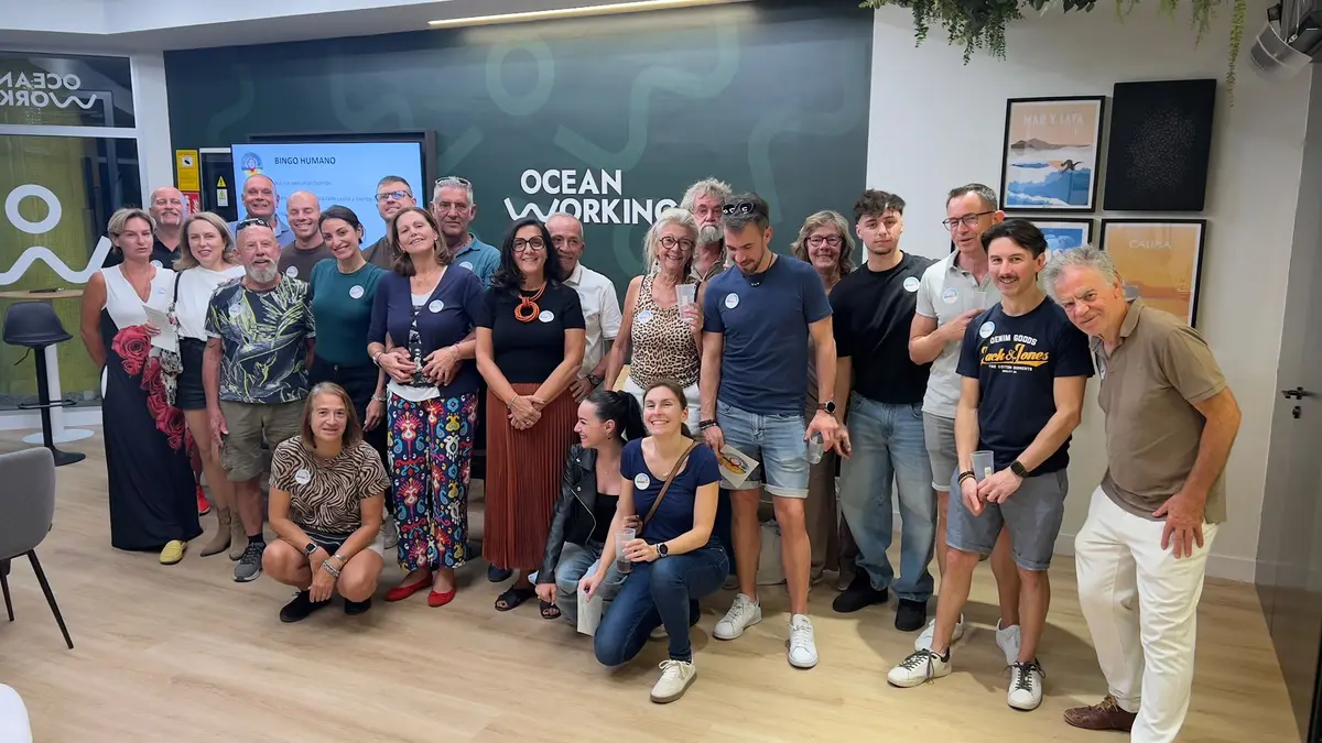 Grupo numeroso reunido en un evento de la comunidad Oceanworking ante la pared con el logo