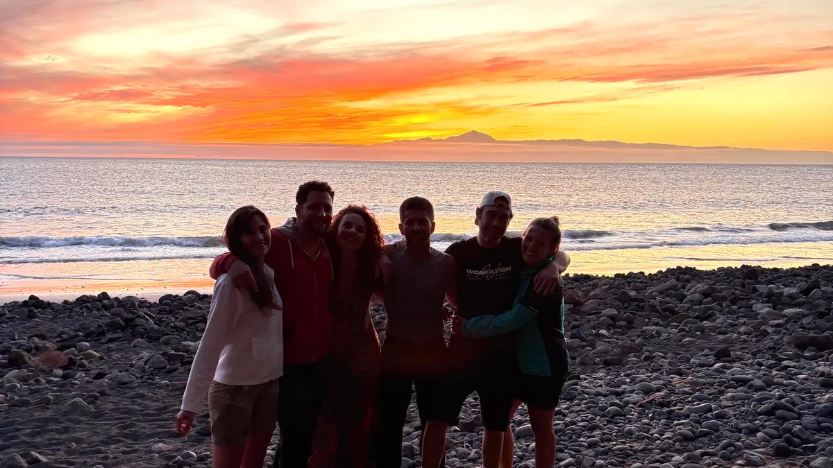 Grupo de amigos abrazados en una playa rocosa al atardecer con el océano de fondo en Gran Canaria