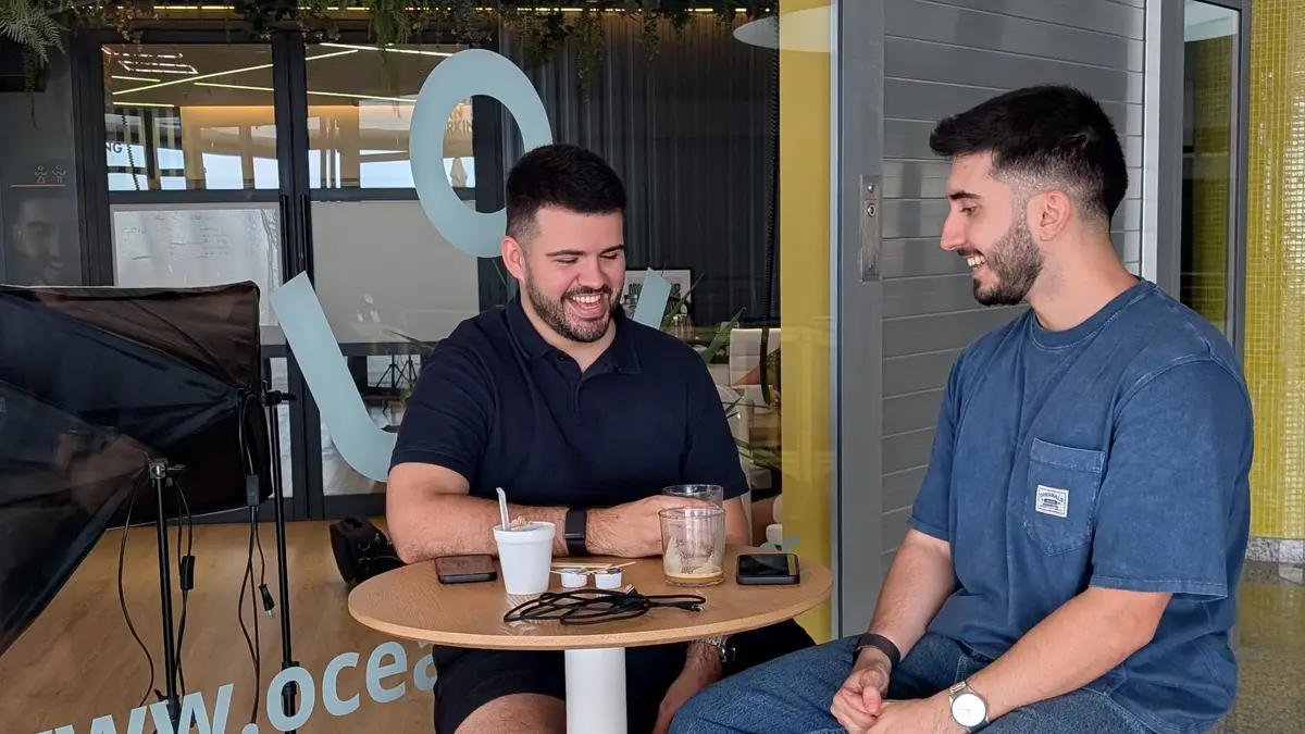 Dos compañeros charlan sonrientes en una mesita de la terraza del coworking Oceanworking