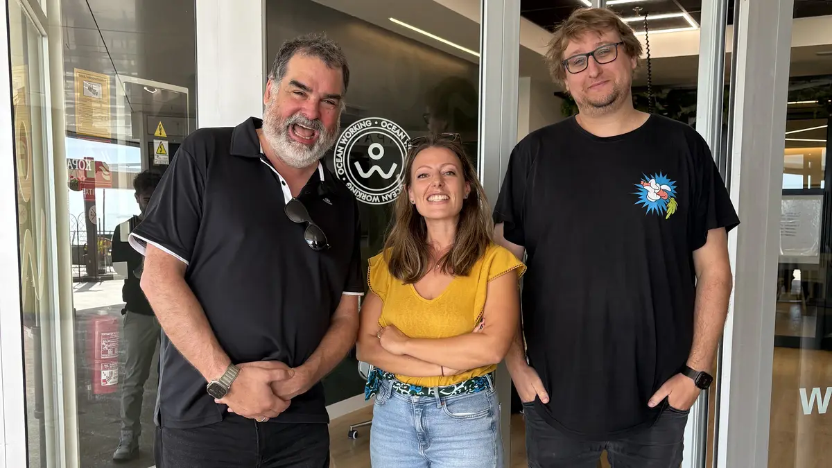 Tres miembros de la comunidad sonríen en la entrada acristalada del coworking Oceanworking