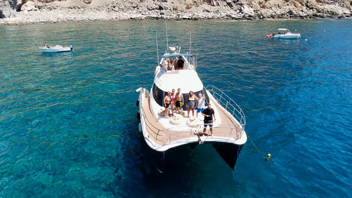 Grupo a bordo de un yate fondeado en una bahía turquesa cerca de los acantilados de Gran Canaria
