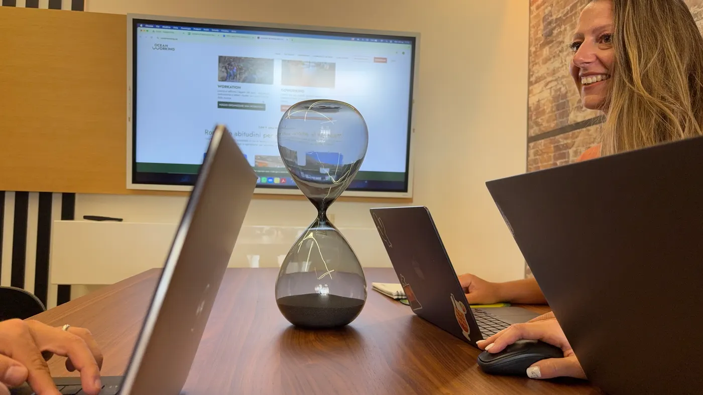 Personas trabajando con portátiles en una sala de reuniones de OceanWorking con un reloj de arena sobre la mesa