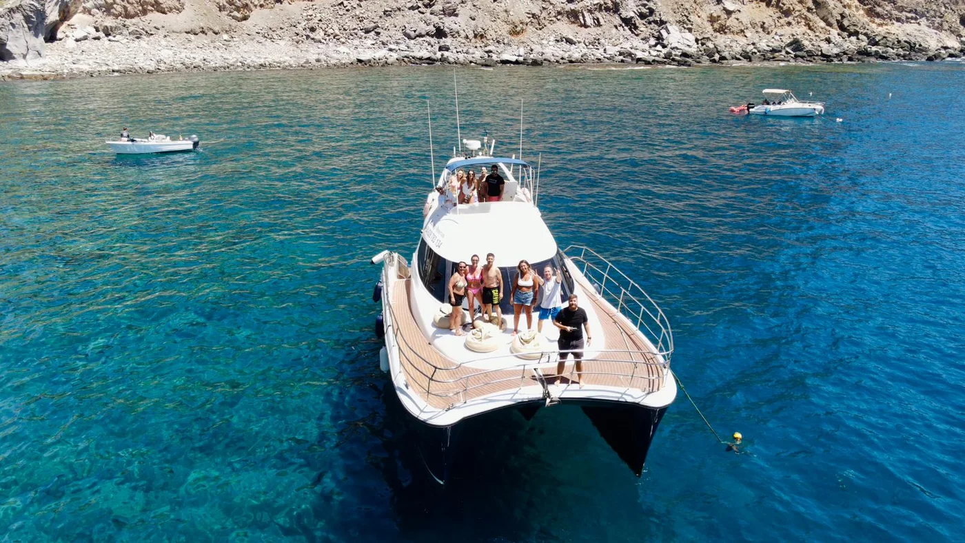 Grupo a bordo de un yate fondeado en una bahía turquesa junto a los acantilados de Gran Canaria