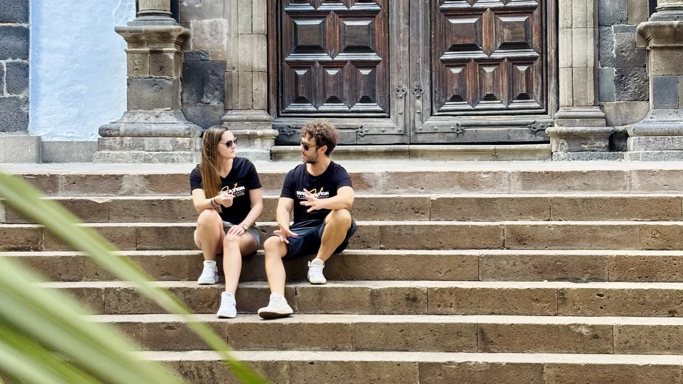 Dos personas hacen una pausa para el café en las escaleras de un edificio histórico de un pueblo de Gran Canaria