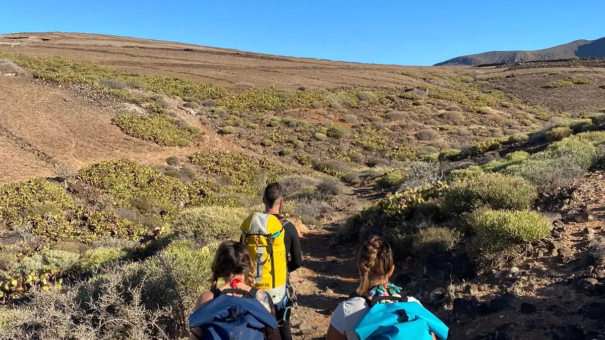 Grupo de senderismo por un sendero en el paisaje volcánico de Gran Canaria con un guía que señala el camino