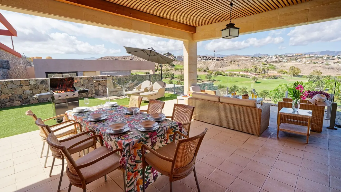 Terraza cubierta con mesa de comedor y zona lounge frente al campo de golf en Gran Canaria