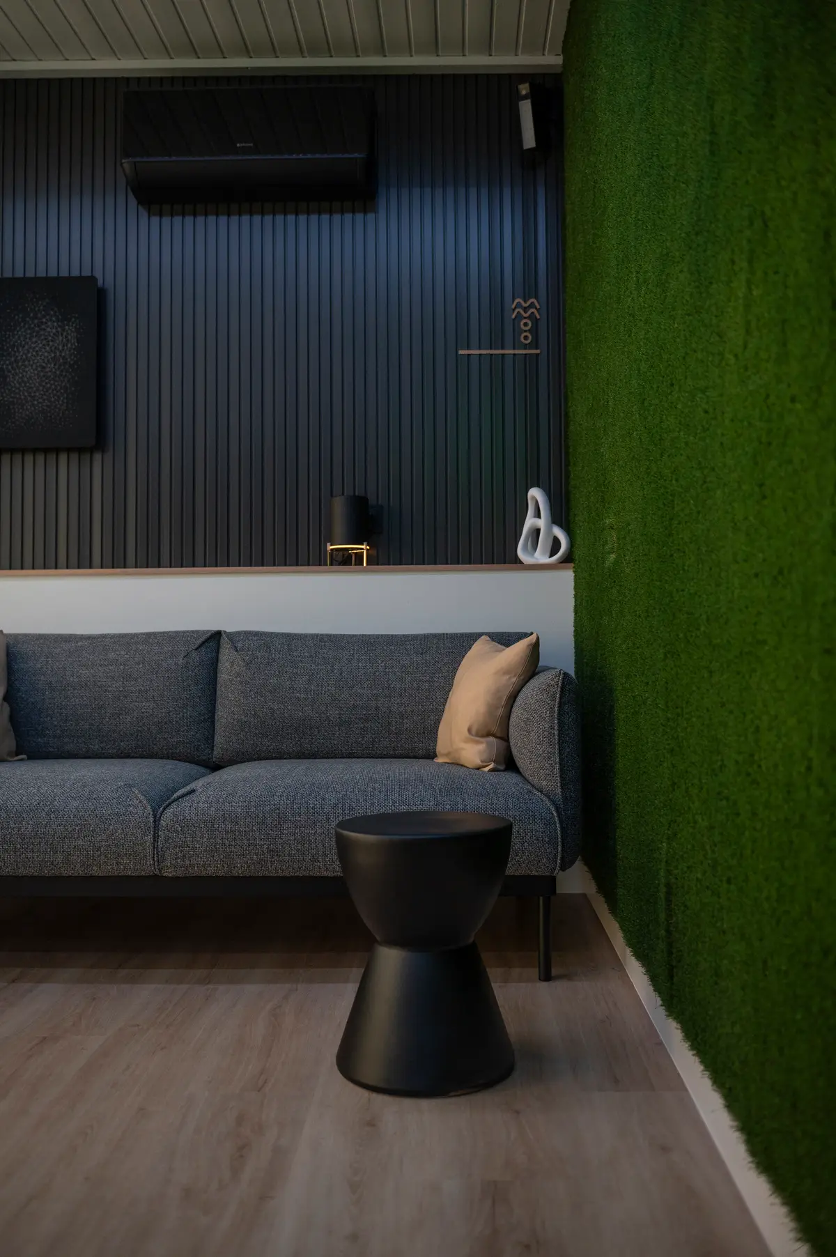 Zona lounge del coworking con sofá gris y pared de césped verde