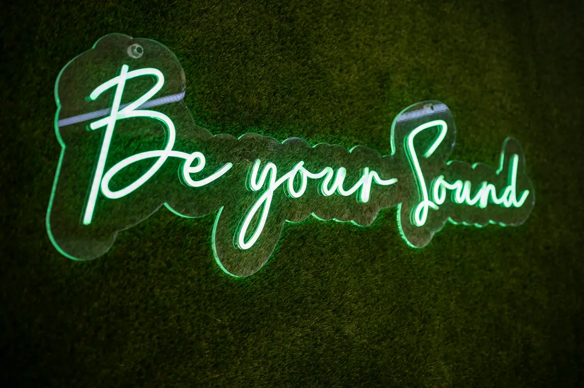 Rótulo de neón 'Be your sound' sobre una pared de césped verde en la sala de podcast