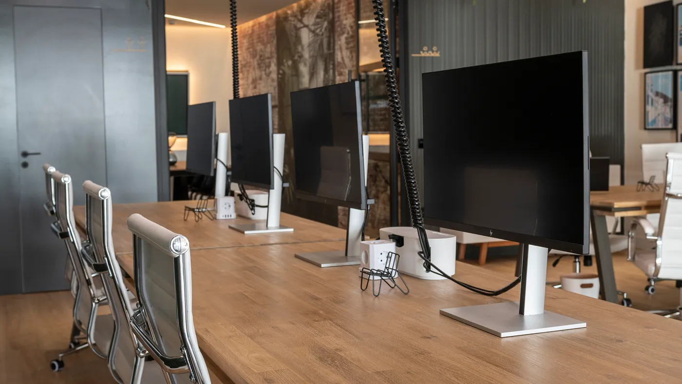 Sala de coworking con monitores alineados sobre una mesa de madera y sillas ergonómicas blancas